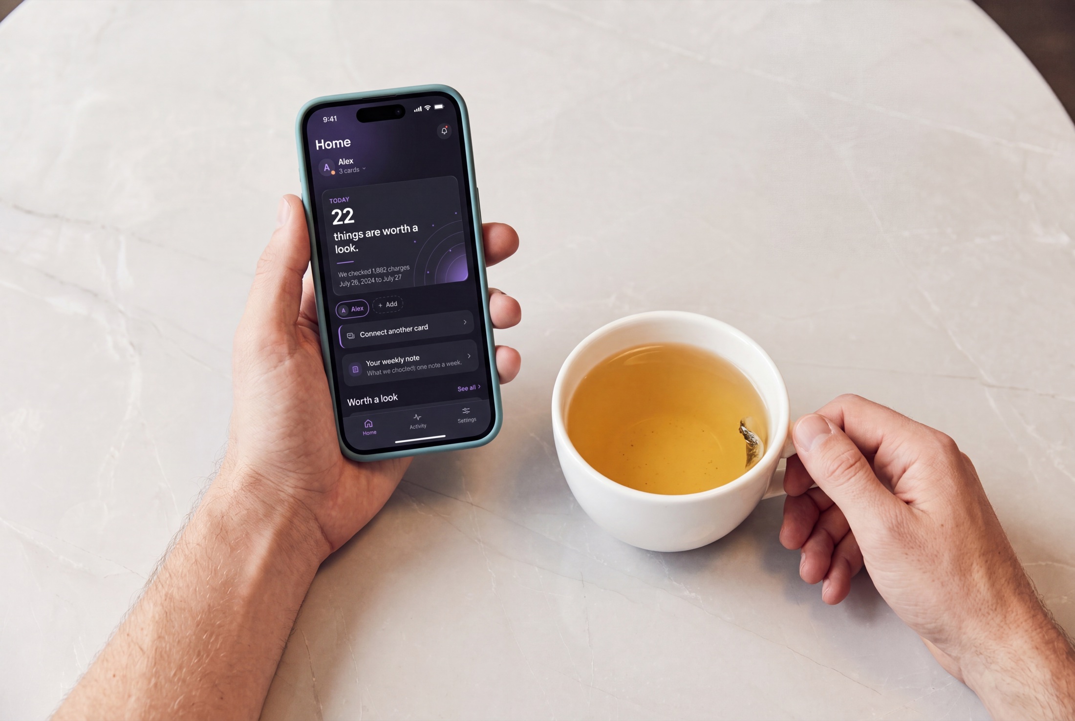 A person holding a phone showing Guardian beside a cup of tea